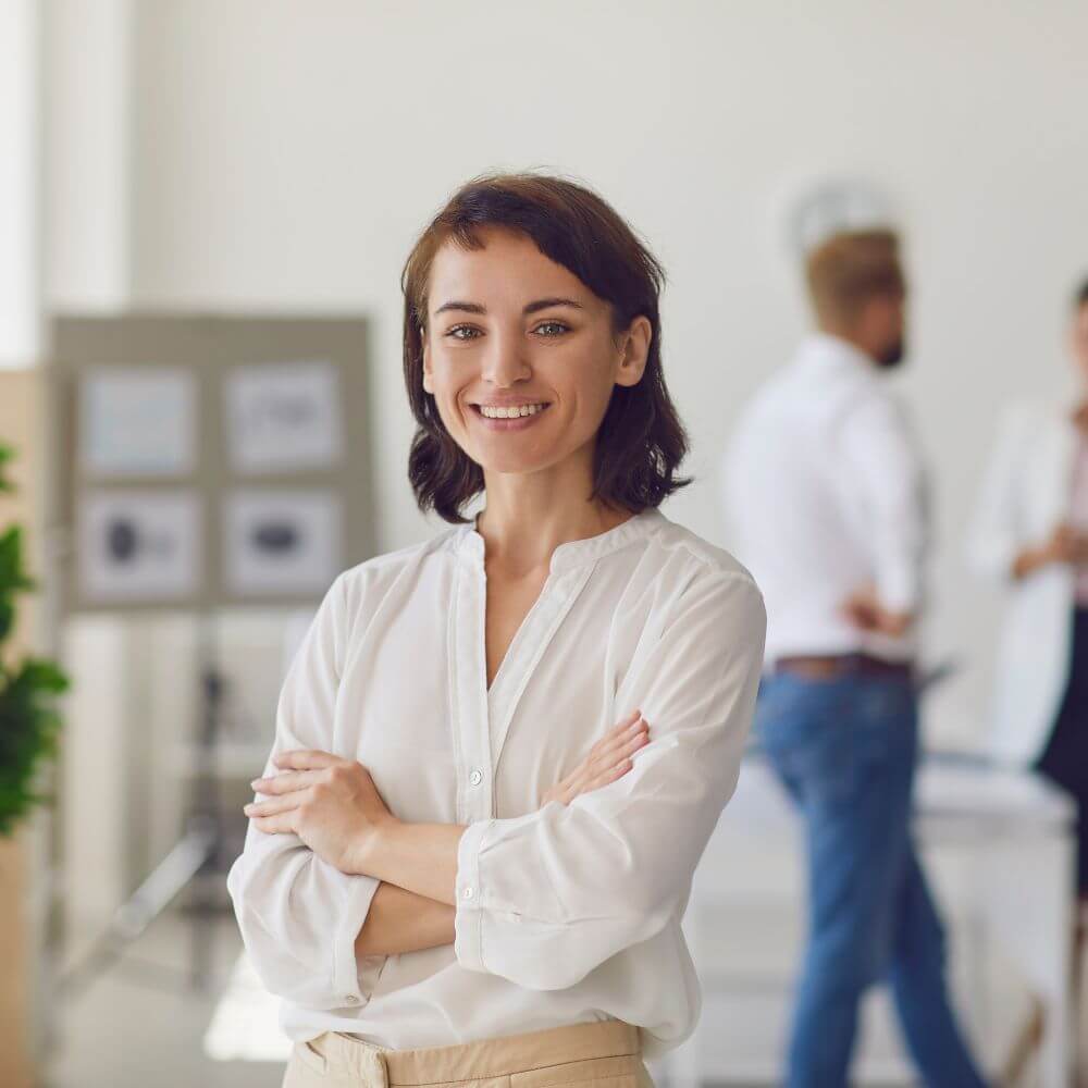business woman smiling arms crossed office in background