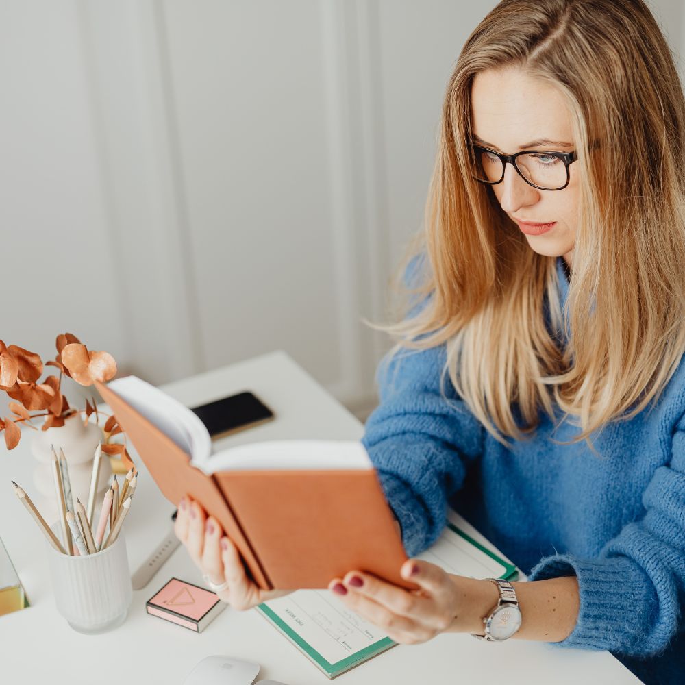 woman reading a book with a peach cover at her desk